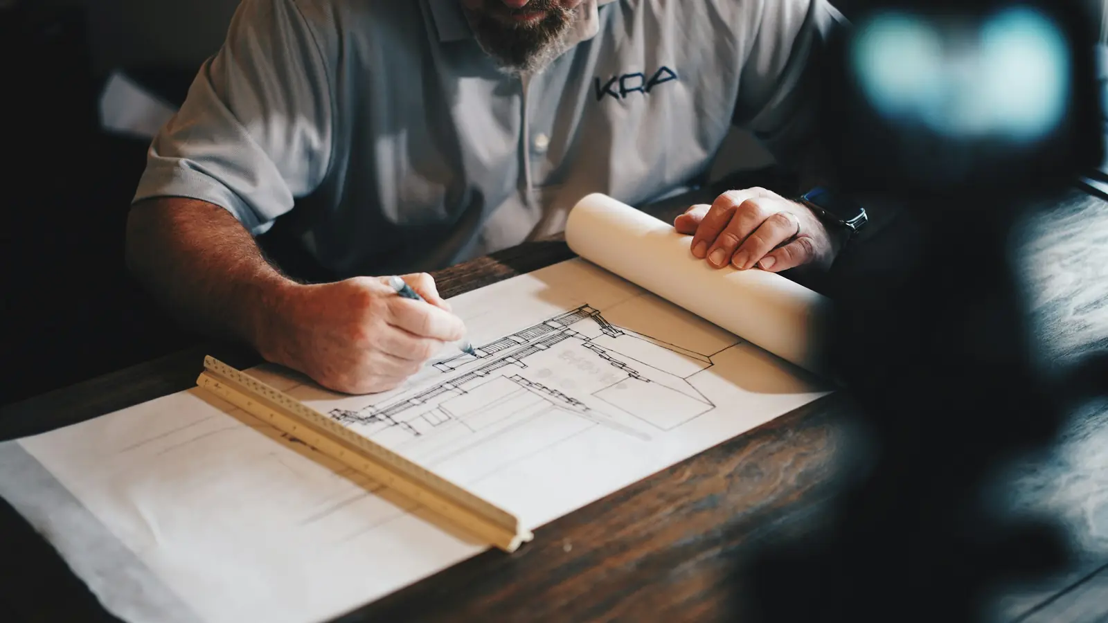 A designer drafting a floor plan by hand with a scale ruler