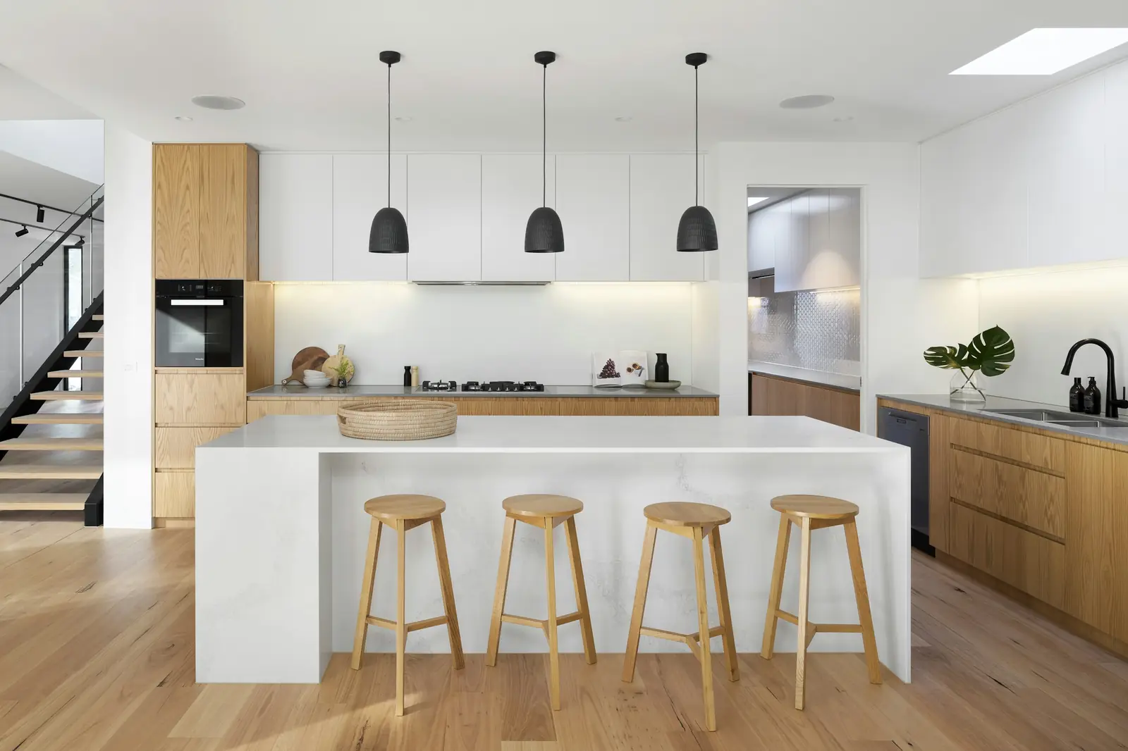 A bright kitchen with white cabinetry, oak stools and pendant lights